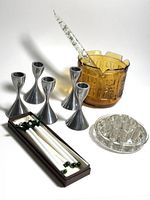 Five metal Umbra candlestick holders, amber glass planter, clear lucite candle, clear glass flower frog, and cocktail picks on white background.