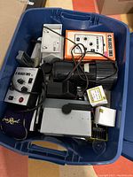 Top-down photo of bin containing various vintage darkroom items including timers, black camera/enlarger, and other boxes.