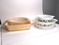 Two Fire King Peach Lustre baking dishes (oval and rectangular) and two Pyrex Daisy patterned bowls.