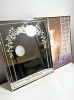 Two framed pieces side by side: a vintage mirror with floral etching and an Art Deco floral print with geometric window