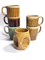 Stacked and grouped image of five ceramic mugs and one owl-shaped mug arranged for display showing glaze colors and profile shapes