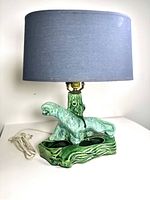 Full view of ceramic panther lamp with grey fabric lampshade and electrical cord on white background.