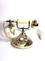 Front view of vintage rotary phone with brass finish and ivory handset, showing rotary dial and base