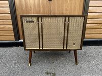 Front view of the vintage Electrohome record player cabinet showing fabric speaker cover, wooden sides and legs, with Electrohome badge.