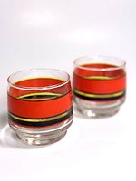 Two vintage rocks glasses with a thick orange band and smaller black, yellow, and gold stripes, shown side by side on white surface.