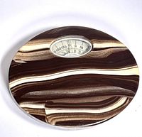 Top view of the vintage weight scale showing the oval marbled plastic casing in brown and cream swirls with the analog dial window.