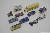 Top view of all 11 miniature toy vehicles arranged on a white surface, showing various vehicle types and colors.