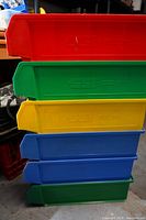 Stack of 6 hopper bins in various colors stacked vertically showing their size and colors.
