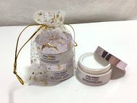 Two Shiseido White Lucent Brightening Moisturizing Cream 18ml jars, one jar open showing white cream inside, both in small mesh bag with gold star pattern.