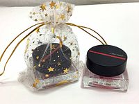 Shiseido blush in square glass pot inside and outside a decorative gold star mesh gift bag with drawstring closure.