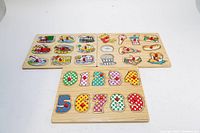 Set of three wooden puzzles displayed: numeric puzzle at front, and two other puzzles with food and transport themes in background, showing missing pieces.