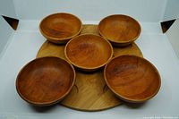Five round wooden bowls displayed on a round bamboo tray, showing wood grain and natural finish.