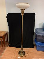 Full view of brass floor lamp with glass shade, cord visible on floor