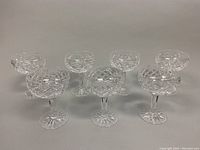 Seven Waterford crystal champagne glasses arranged in two rows on a neutral surface showing full set.