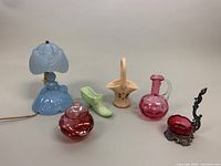 Full view of all items including the blue lamp, red glass covered jar, green glass shoe figurine, cream Westmoreland basket, pink glass pitcher, and decorative metal and glass box