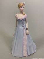 Front view of the porcelain figurine in a blue and pink gown holding a bouquet, showing facial details and full gown.