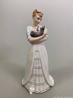 Front view of 9-inch Royal Doulton porcelain figurine showing woman holding cat in white and blue dress with detailed facial features.
