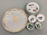 Set of plates including one large 12-inch gilded cake plate and eight smaller dessert plates with fruit illustrations