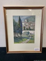 Framed watercolour showing the full artwork with a village scene, cypress trees, and landscape under glass in a gold-tone frame.