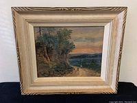 Full view of framed watercolour painting showing landscape scene with dirt road, rocky cliff, and distant town under sunset sky.