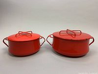 Front view of two red enameled covered casserole pots, one larger and one smaller