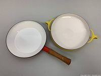 Both pans viewed from top showing enamel interior and bright exterior colors; red skillet and yellow paella pan