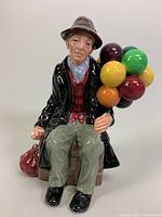 Front view of Royal Doulton Balloon Man figurine showing seated man holding colorful balloons and small bag beside him.