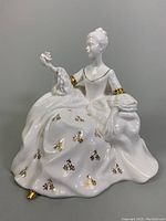 Front and side view showing the seated female figurine holding a bird with detailed gold floral designs on dress.