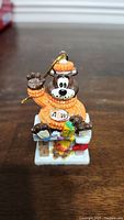 Front view of A&W Bear Christmas Ornament sitting on chimney, wearing orange sweater and hat with A&W logo, waving one hand.
