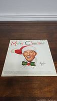Front cover of Bing Crosby Merry Christmas vinyl record showing Bing Crosby wearing a Santa hat and colorful 'Merry Christmas' text.