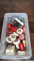 Top view of clear plastic container filled with assorted red, white, and green Yankee Candle wax tarts in flower shapes with some scent labels visible.