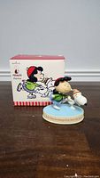 Figurine with box behind showing Lucy skating with Snoopy, side view