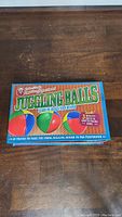 Top view of the kit box showing colorful juggling balls and text indicating a how-to-juggle kit with 3 balls and a book inside.