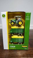 Front view of boxed John Deere 7290R die-cast tractor and two forage wagons showing the items inside the clear window.
