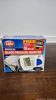 Front of the Life Manual Blood Pressure Monitor box showing the product, digital display, cuff, and bulb with brand and product name.