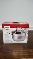 Box of new 4 quart stainless steel Dutch oven with glass lid and stainless steel handles shown from front
