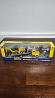 Front view of the boxed New Holland construction vehicle set showing the vehicles and traffic signs.