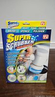Front view of the Super Scrubber box showing product name, features, and images of the device with interchangeable heads.
