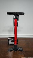 Full view of the new Supercycle brand bicycle pump showing red barrel, black handle, hose, and foot pedals.