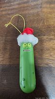 Front view of the Pickle Rick Santa Christmas ornament showing the face and Santa hat with hanging string loop
