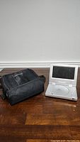 Protron portable DVD player open showing screen and DVD tray, next to black carrying case on wooden floor.