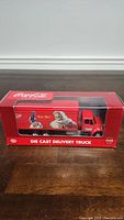 Front and side view of the boxed die-cast Coca-Cola delivery truck showing Santa Claus artwork on trailer.