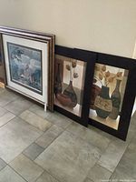 Three framed prints leaning against the wall, including the large AJ Casson print and two smaller still life prints.