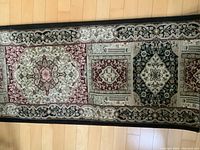 Close-up of carpet runner showing medallion and floral design patterns in red, black, beige and cream colors on wooden floor.
