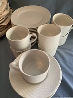 Stack of white textured rim dinner plates, cups, and saucers shown from side angle