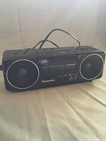 Front view of black Panasonic ATS clock radio showing central display and two circular speakers with white trim.