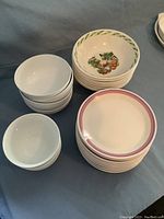 Set showing stacked luncheon plates with pink rim, medium vegetable motif pasta bowls, and smaller white bowls.