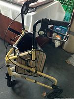 Three-quarter angle view of yellow three-wheeled foldable walker featuring front and rear wheels, plaid fabric basket, black rubber handles, and brake cables.