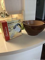 Sunbeam Mixmaster handheld electric mixer displayed in original packaging box with two brown plastic mixing bowls on counter