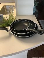 Three T-Fal frying pans stacked, showing black non-stick interiors and handles